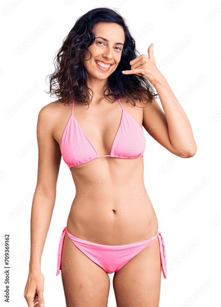 Young beautiful hispanic woman wearing bikini smiling doing phone gesture with hand and fingers like talking on the telephone. communicating concepts. Young beautiful hispanic woman wearing bikini smiling doing phone gesture with hand and fingers like talking on the telephone. communicating concepts.