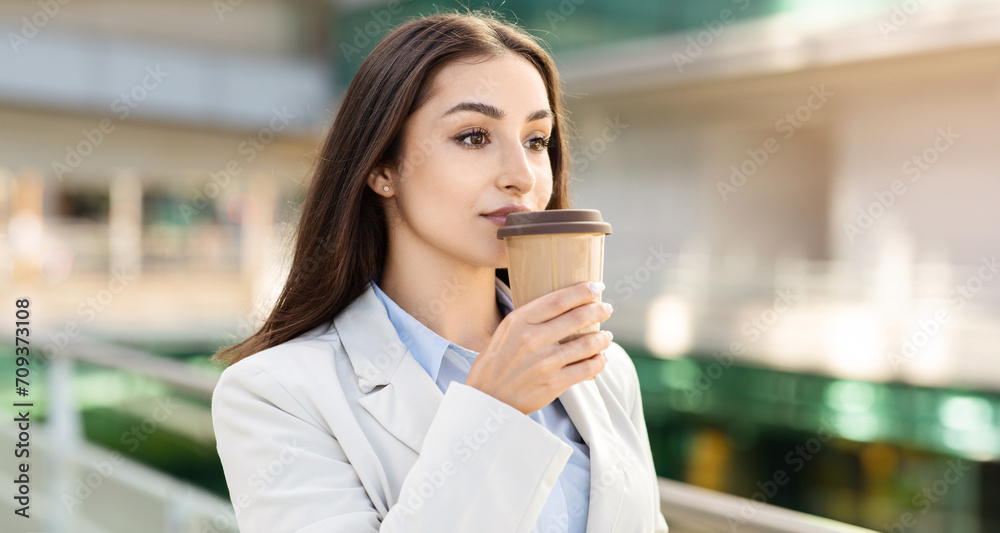 Focused businesswoman sipping coffee from a takeaway cup Focused businesswoman sipping coffee from a takeaway cup