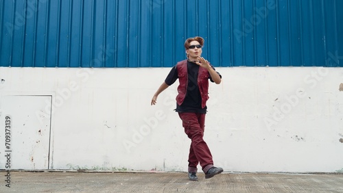 Handsome street dancer practicing break dancing at white back ground. Sport man wearing hip hop style while moving footsteps to music at street with blue background. Outdoor sport 2024. Endeavor. © Summit Art Creations