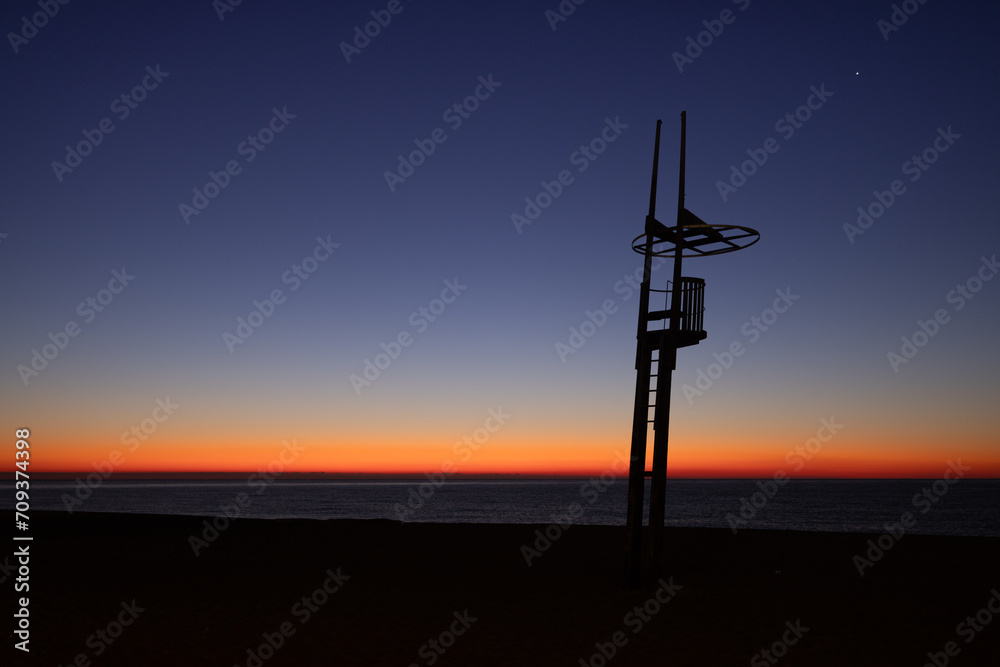 Fototapeta premium Dawn on a Mediterranean beach with the silhouette of the lifeguard tower
