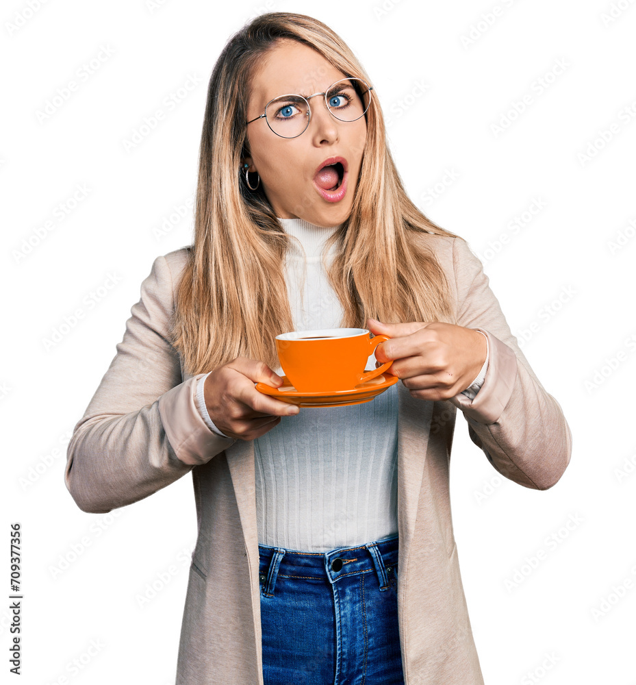 Young blonde woman wearing business style drinking cup of coffee in shock face, looking skeptical and sarcastic, surprised with open mouth Young blonde woman wearing business style drinking cup of coffee in shock face, looking skeptical and sarcastic, surprised with open mouth