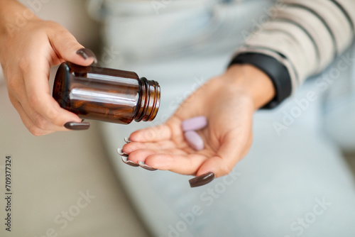 Focused image of a woman at home pouring purple pills into her hand from a brown medicine bottle