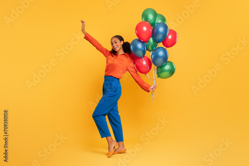 black girl holding bunch of colorful balloons raising arm, studio