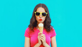 Summer portrait of happy young woman eating ice cream wearing sunglasses on blue background