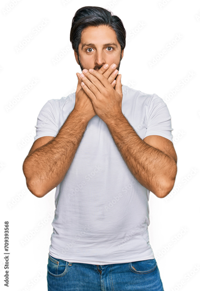 Young hispanic man wearing casual white t shirt shocked covering mouth with hands for mistake. secret concept. Young hispanic man wearing casual white t shirt shocked covering mouth with hands for mistake. secret concept.