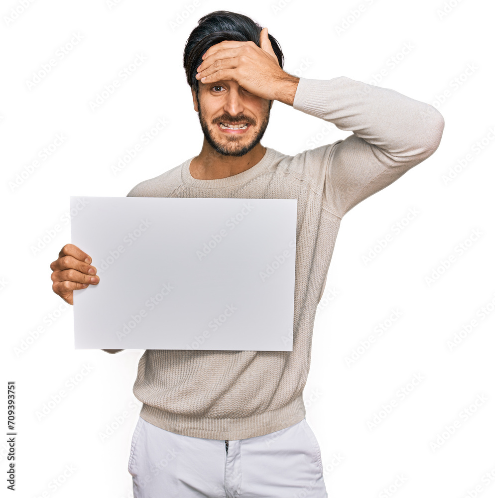 Young hispanic man holding blank empty banner stressed and frustrated with hand on head, surprised and angry face Young hispanic man holding blank empty banner stressed and frustrated with hand on head, surprised and angry face