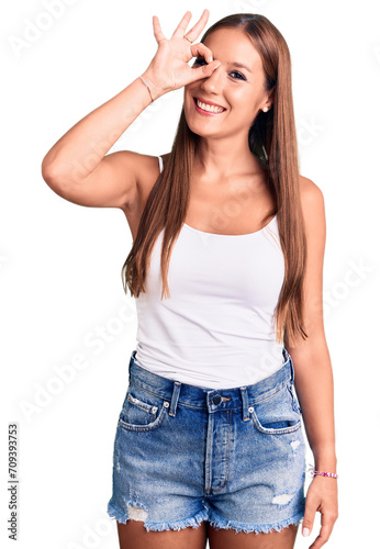 Young beautiful hispanic woman wearing casual clothes smiling happy doing ok sign with hand on eye looking through fingers