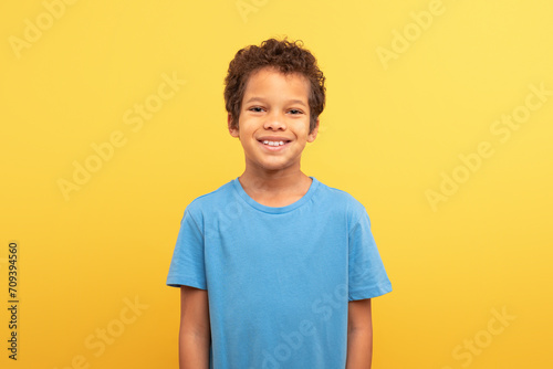 Portrait of smiling boy in blue shirt against yellow background