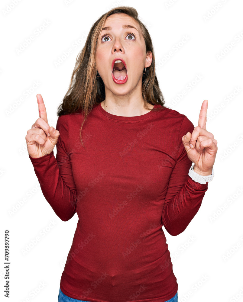 Young blonde woman wearing casual clothes amazed and surprised looking up and pointing with fingers and raised arms. Young blonde woman wearing casual clothes amazed and surprised looking up and pointing with fingers and raised arms.