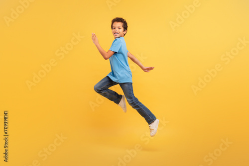 Black boy in mid-run on bright yellow background © Prostock-studio