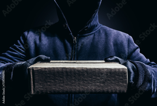 Obraz na plátne Photo of scary shaded hooded man giving a cardboard box parcel on dark background