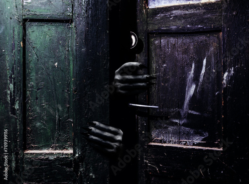 Photo of old obsolete and shaded abandoned grungy door with scary female monster hands with claws reaching out from darkness.