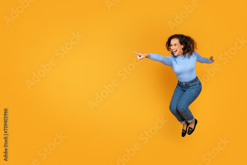 Cheerful excited young woman jumping on yellow, copy space © Prostock-studio