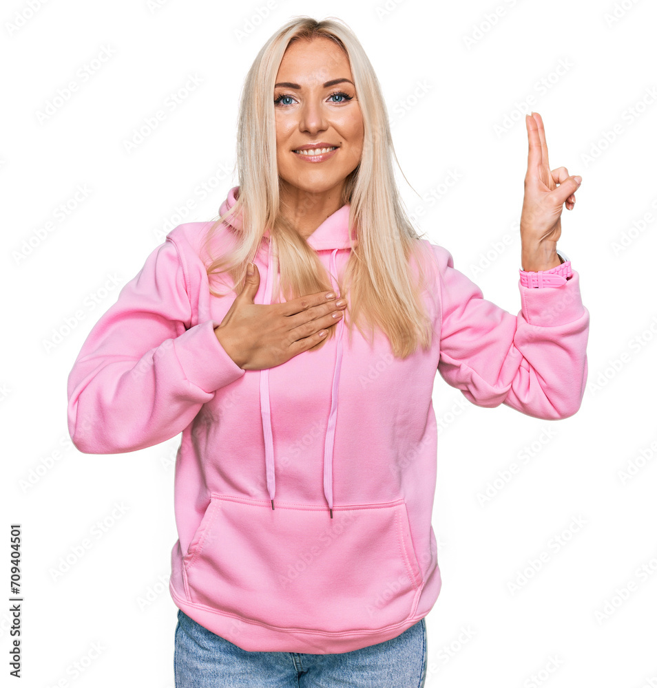 Young blonde woman wearing casual sweatshirt smiling swearing with hand on chest and fingers up, making a loyalty promise oath Young blonde woman wearing casual sweatshirt smiling swearing with hand on chest and fingers up, making a loyalty promise oath