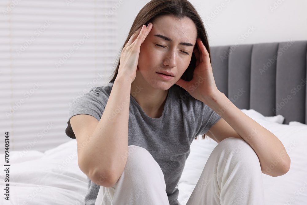 Sad woman suffering from headache on bed indoors Sad woman suffering from headache on bed indoors