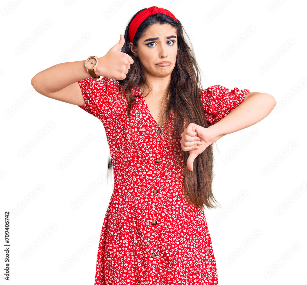 Brunette teenager girl wearing summer dress doing thumbs up and down, disagreement and agreement expression. crazy conflict Brunette teenager girl wearing summer dress doing thumbs up and down, disagreement and agreement expression. crazy conflict