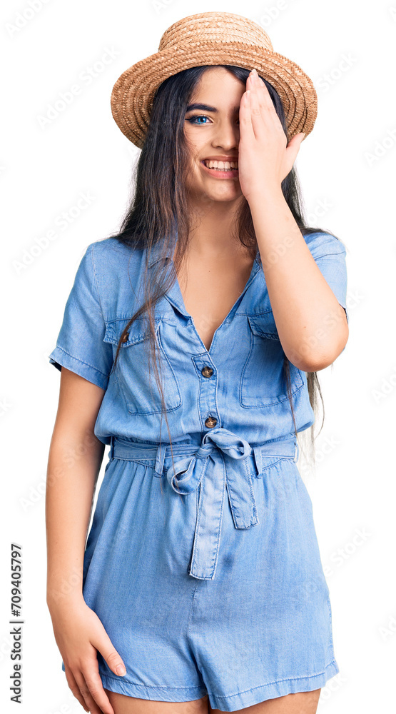 Brunette teenager girl wearing summer hat covering one eye with hand, confident smile on face and surprise emotion. Brunette teenager girl wearing summer hat covering one eye with hand, confident smile on face and surprise emotion.