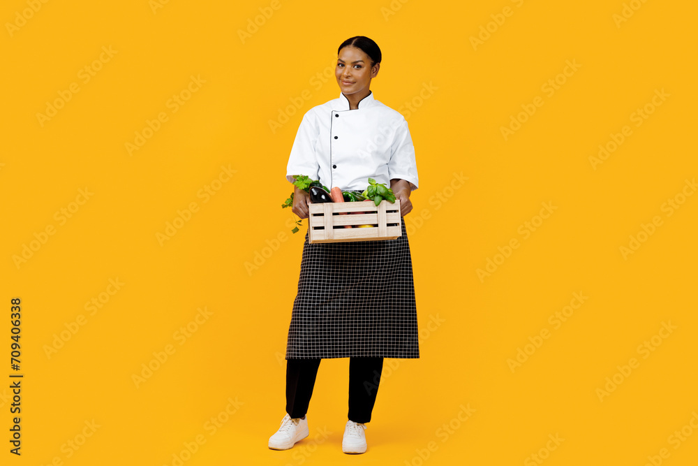 Smiling black female chef presenting wooden crate of organic vegetables Smiling black female chef presenting wooden crate of organic vegetables