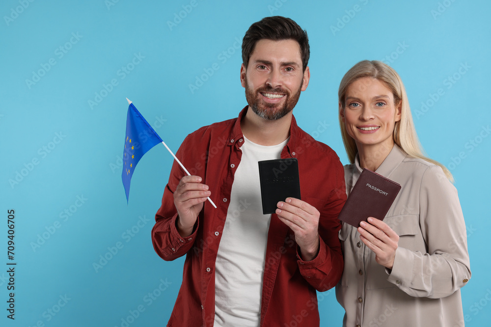 Immigration. Happy couple with passports and flag of European Union on light blue background Immigration. Happy couple with passports and flag of European Union on light blue background