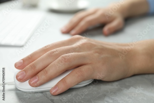 Woman using wired computer mouse at light grey marble table  closeup