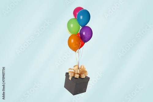 Many balloons tied to gift box on light blue background photo