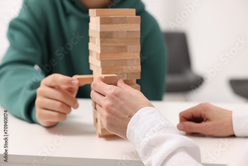 People playing Jenga tower at white table indoors, closeup