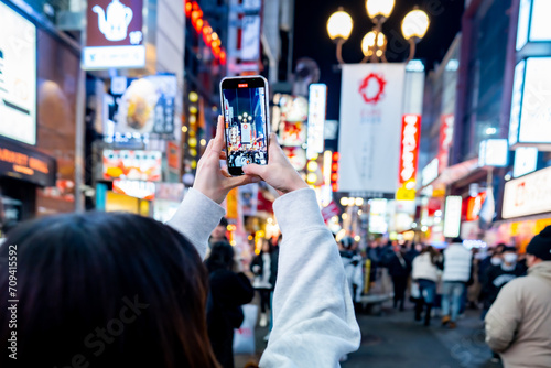 female tourist taking a photo with the famous night shopping street food at Dotonbori or dotombori, Dotonbori the famous destination for traveller in Shinsaibashi, Osaka City, Osaka, Japan.