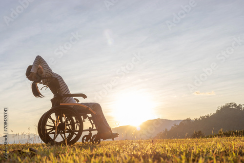 Silhouette Girl in wheelchair looking sunset mountain background.