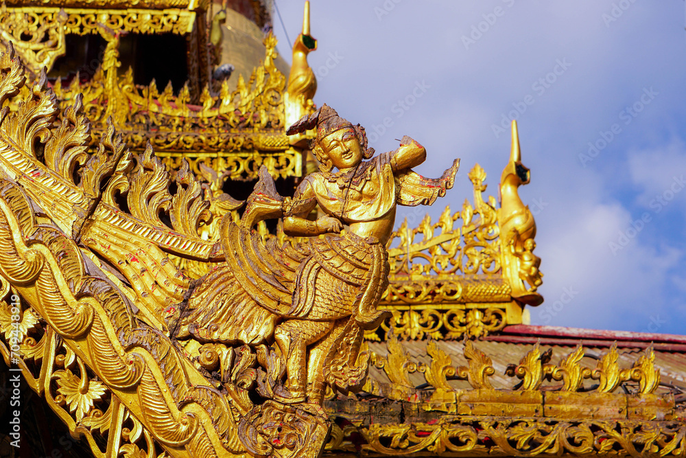 Fototapeta premium Closeup and crop antique golden carved wood Burmese art on the roof of the Burmese temple chapel in Lampang province, Thailand.