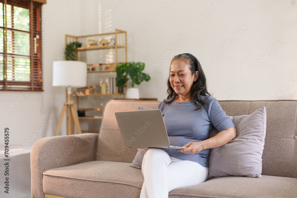 Senior asian woman sitting on sofa using laptop computer, working, chatting, social media internet at home. Senior asian woman sitting on sofa using laptop computer, working, chatting, social media internet at home.