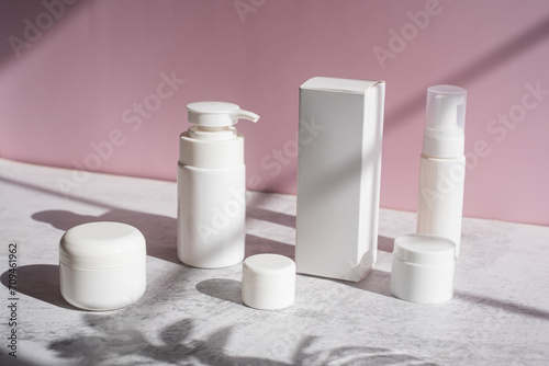 The white skincare set with pump, jar, and box and container on pink background.