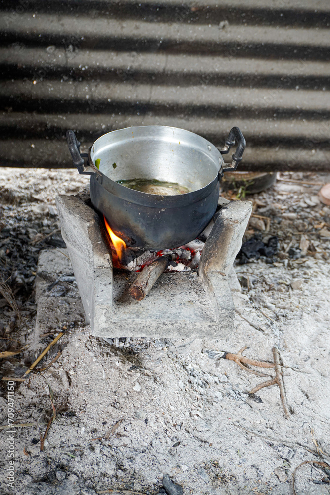 An old pot black and dented placed on top of old stove in the style of the countryside, using logs (firewood) to light the fire for cooking. There was a pile of ashes in front. An old pot black and dented placed on top of old stove in the style of the countryside, using logs (firewood) to light the fire for cooking. There was a pile of ashes in front.