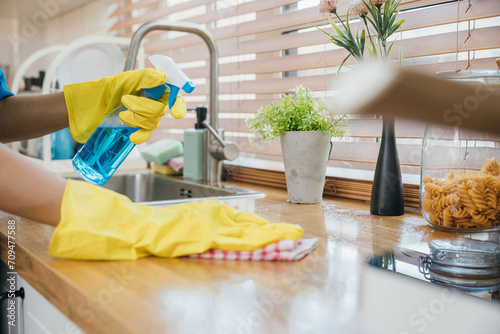 Maid in uniform working with spray bottle cleaning kitchen worktop. Emphasizing hygiene and safety in housekeeping. Portrait of employee caring for home purity. Clean disinfect home care. Give me.