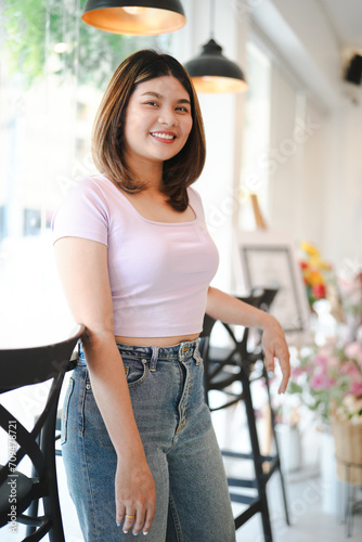 Side view of happy asian woman standing alone in cafe near window, smiling on summer sunny day, wearing t-shirt with jeans.