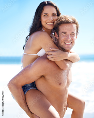 Portrait, piggy back and happy couple at ocean for holiday adventure together on tropical island on blue sky. Smile, man and woman on beach vacation with waves, hug or love on romantic travel in Bali photo