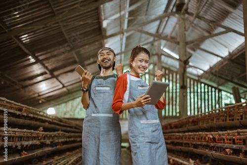 smiling entrepreneur man and woman with celebrate gesture holding tablet and cell phone at chicken farm