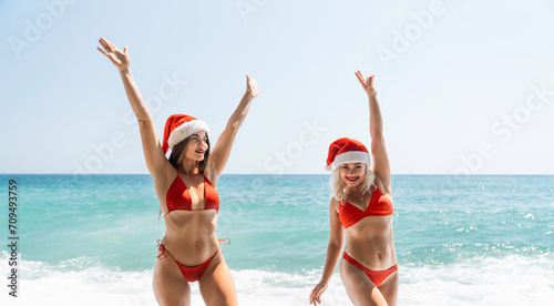 Women in Santa Claus hats run into the sea dressed in red swimsuits. Celebrating the New Year in a hot country
