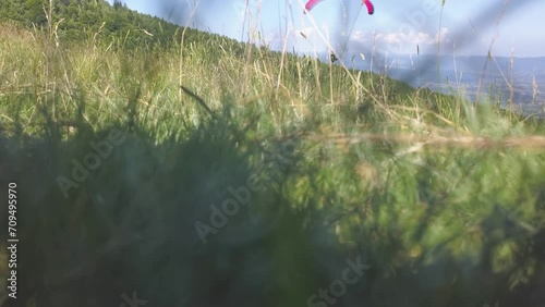 Paraglider flying left to right toward valley below. Pilor soaring on air. Low angle view from the ground, behind grass. photo