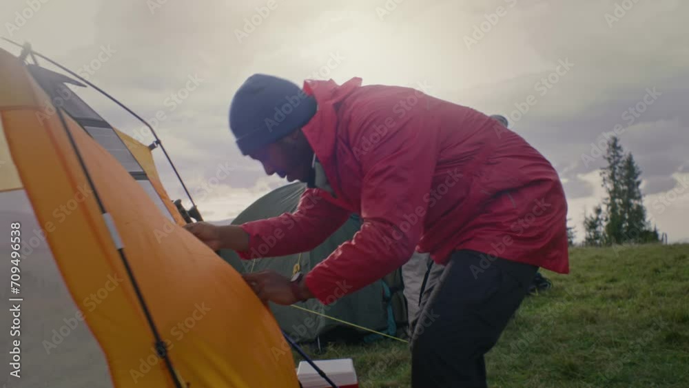 Multi ethnic group of outdoor enthusiasts set up camping. African American male traveler closes tent. Tourists stopped to rest after long expedition. Nature discovery and tourism concept. Slow motion. Multi ethnic group of outdoor enthusiasts set up camping. African American male traveler closes tent. Tourists stopped to rest after long expedition. Nature discovery and tourism concept. Slow motion.