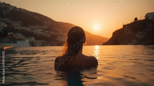 Rear view of woman looking at scenery in swimming pool at sunset, woman traveling in mediterranean sea in summer, woman looking at scenery in luxury hotel swimming pool, faceless travel footage © yuanfeng Z