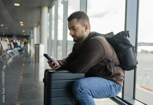 Busy tourist man locating in waiting hall. Young man with cellphone at the airport while waiting for plane