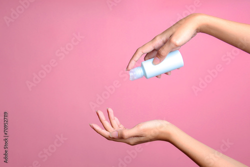 Woman hand pouring lotion from blue blank bottle for mockup over pink pastel background © Queenmoonlite Studio