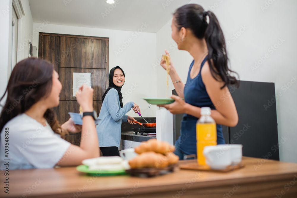 three Asian women laugh while making breakfast and eating together in the kitchen three Asian women laugh while making breakfast and eating together in the kitchen