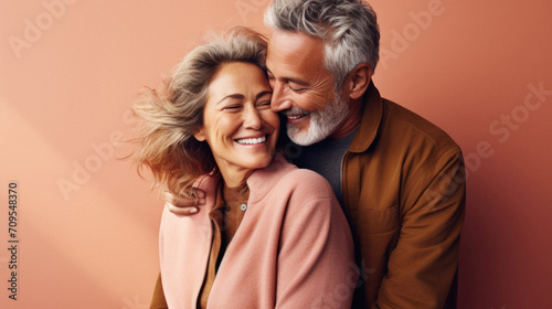 Cheerful senior couple hugging and looking at camera isolated on beige.