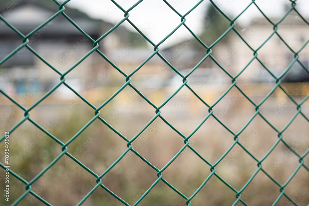 Green metal mesh fence that using to barricade the area, scene with blurred background of city outdoor place. Close-up and selective focus. Green metal mesh fence that using to barricade the area, scene with blurred background of city outdoor place. Close-up and selective focus.