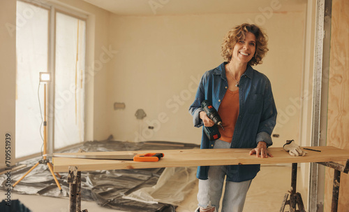 Smiling woman renovating kitchen with drill tool in happy home improvement project