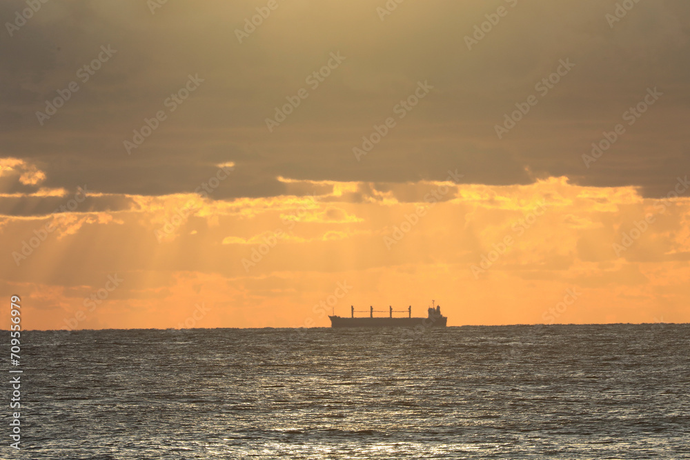 commercial cargo ship sailing in the sun and dark clouds