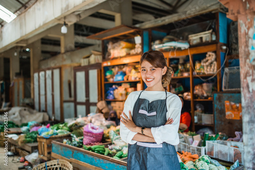 asian female vegetable seller standing in front of vegetables stall smiling with crossed arm photo