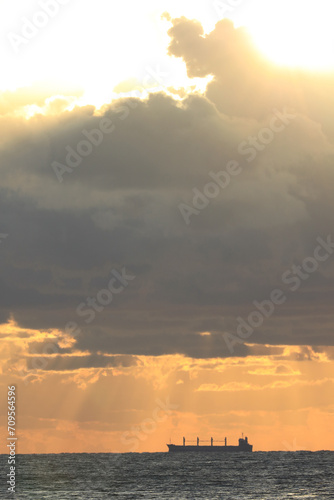 commercial cargo ship sailing in the sun and dark clouds