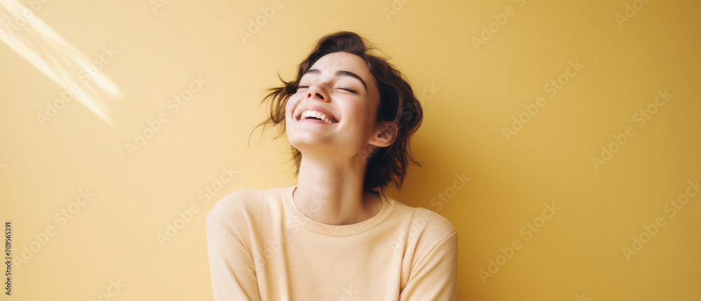 Fototapeta premium Portrait of a beautiful young woman laughing with closed eyes on a yellow background